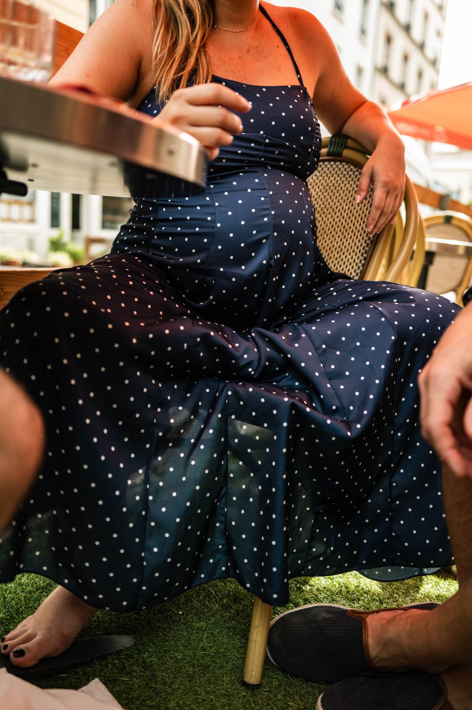 A pregnant woman sitting down, wearing a silky blue dress with white polka dots