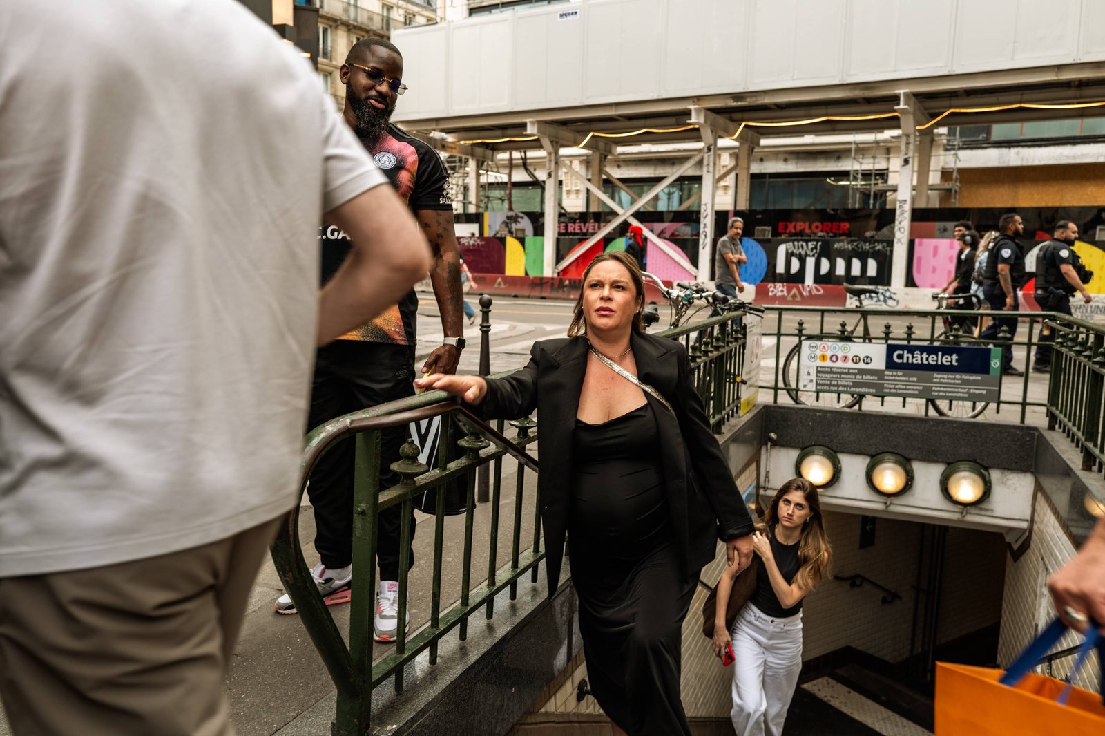 A pregnant woman wearing a silky black dress steps out of the Châtelet subway station amid the crowd