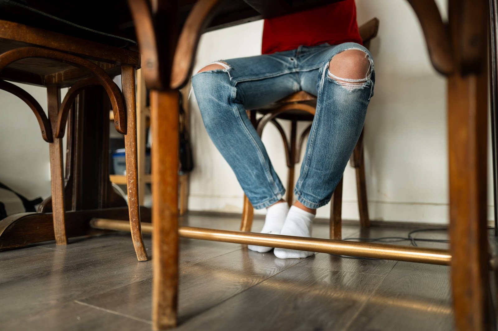 Des jambes en jean déchiré sous une table, pieds en chaussettes blanches.