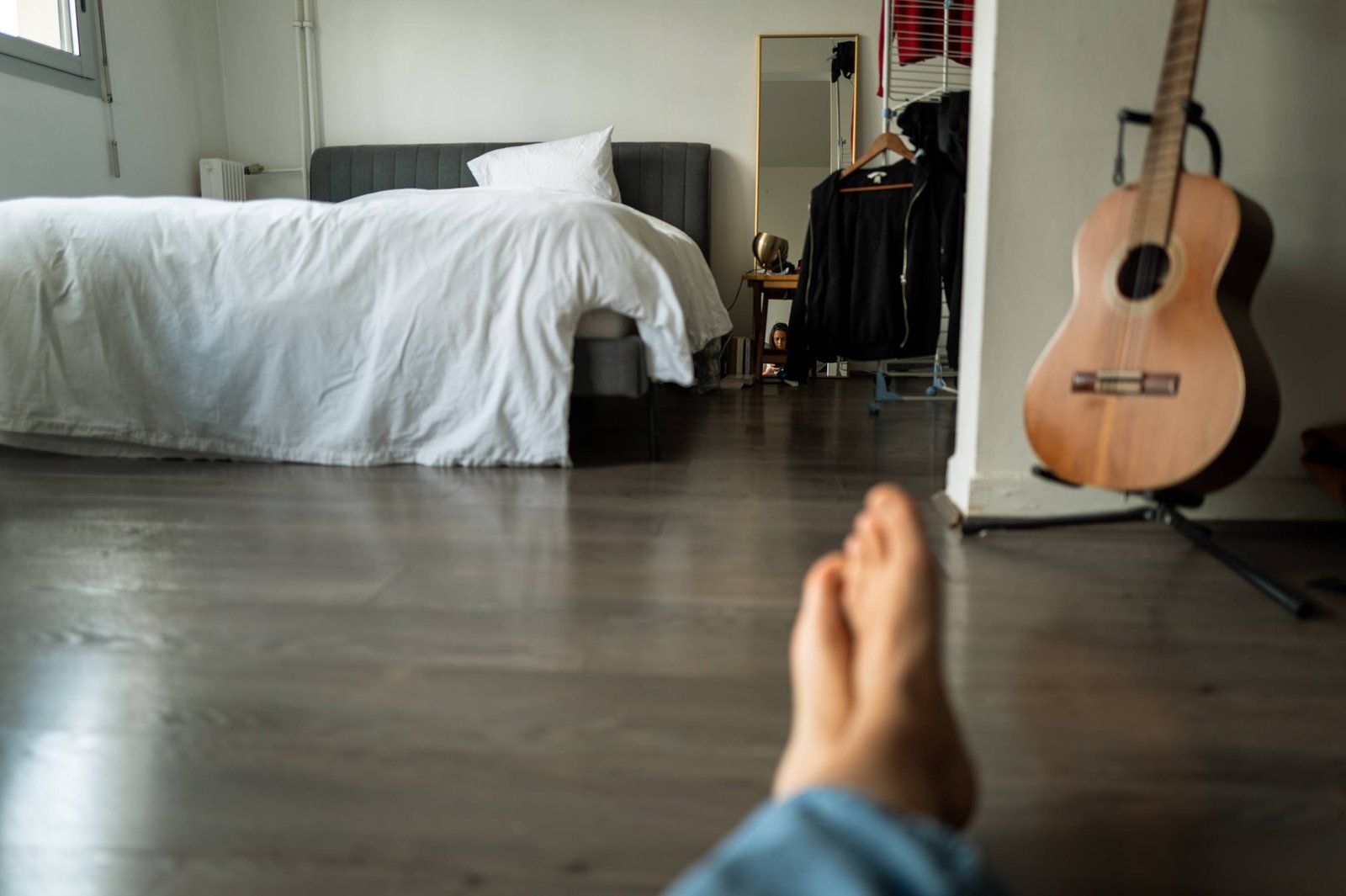 Une chambre avec une guitare, vue derrière un pied nu.