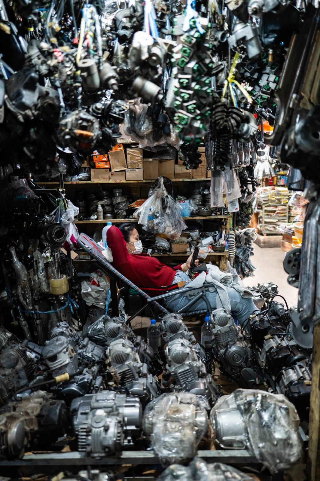 Machines Will Do For Us — Phnom Penh, Cambodia, 2024. A figure absorbed in their phone amid a wall of engines. From Anne Catherine Nobre's Nomophobia series.
