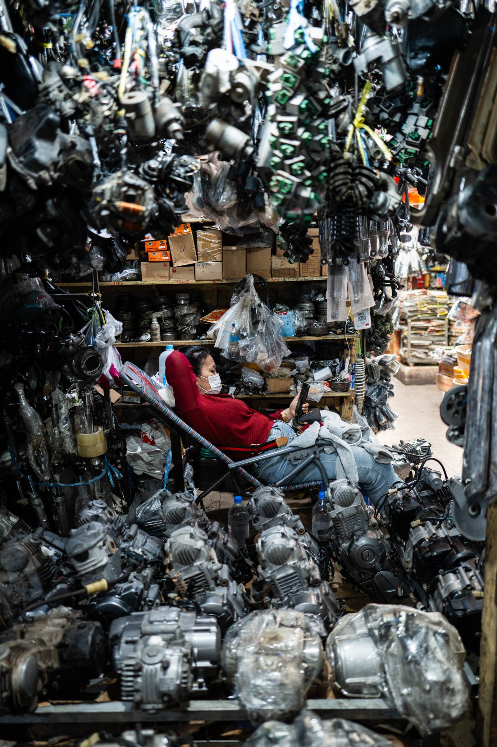 Machines Will Do For Us — Phnom Penh, Cambodia, 2024. A figure absorbed in their phone amid a wall of engines. From Anne Catherine Nobre's Nomophobia series.